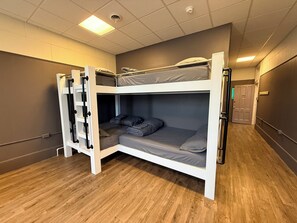 Une chambre avec un lit superposé, une échelle, un plancher en bois et une porte visible au fond.