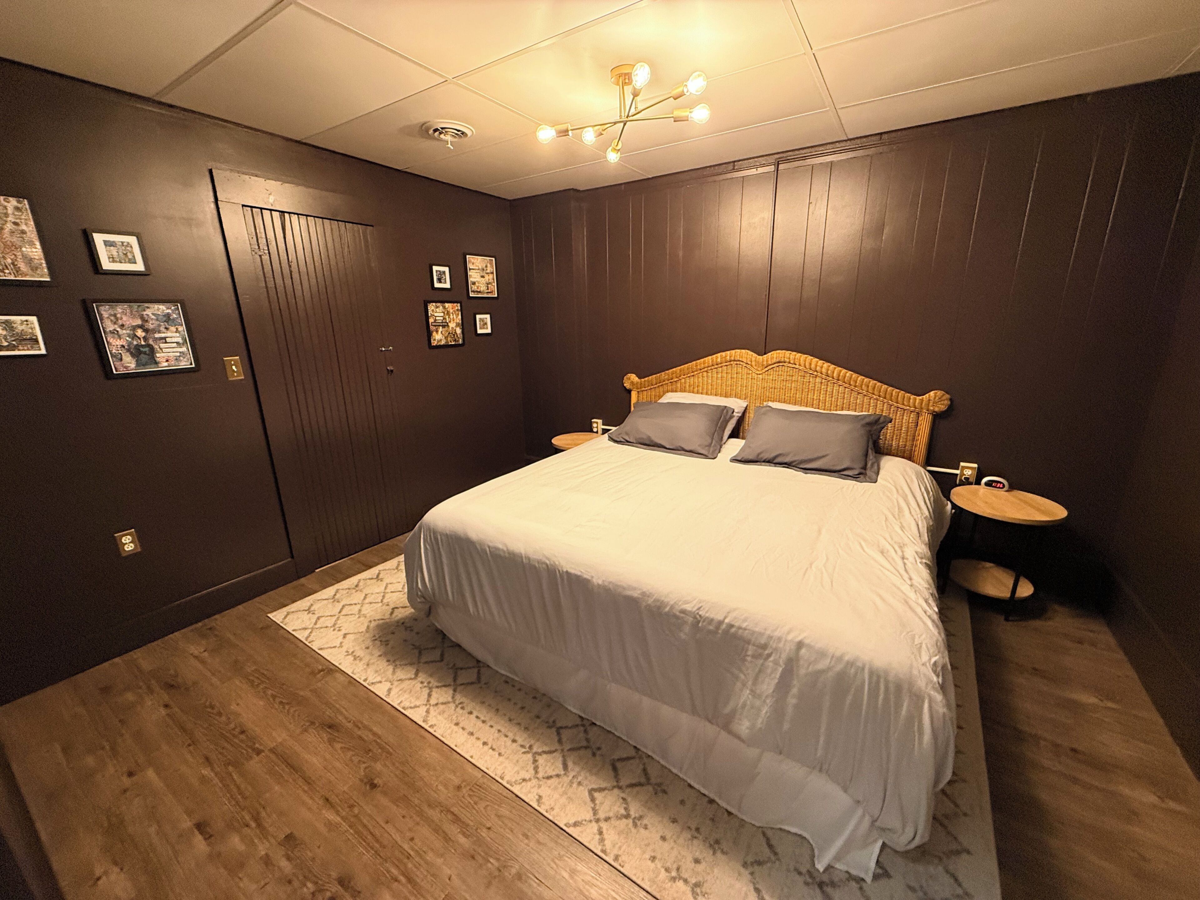 A bedroom with a large bed, dark wooden walls, a ceiling light fixture, and a small bedside table.