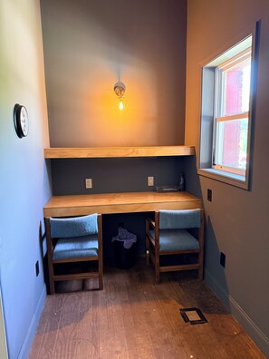 Ein kleines Zimmer mit integriertem Schreibtisch, zwei Stühlen, einer Wandleuchte und einem Fenster mit Blick.