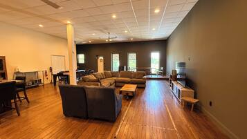 A spacious living area with a large sectional sofa, a dining table with chairs, a television, and a ceiling fan.