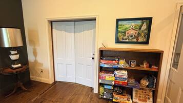 A room with a wooden floor, a white door, a lamp on a table, and a bookshelf with various board games.