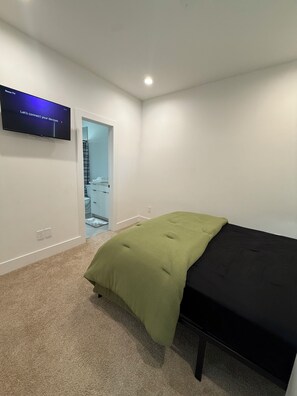 Une chambre à coucher avec un lit, un téléviseur fixé au mur et une porte donnant sur une salle de bain.