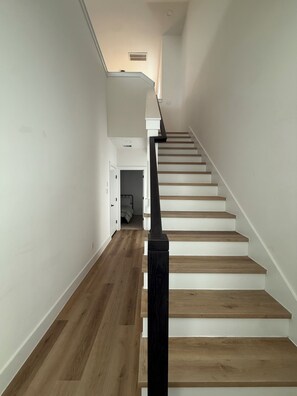 Eine Treppe mit Holzbodenstufen und einem schwarzen Geländer, die zu einer Zwischenebene mit einer Tür führt.