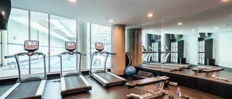 Un gimnasio con cintas de correr, una banca y pesas.