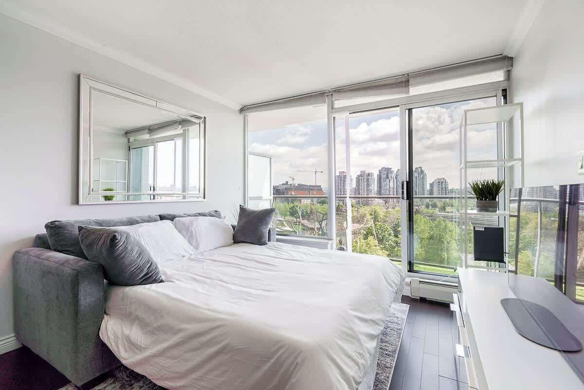 A modern bedroom with a bed, a desk, and a large window with a city view.