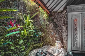 A room with a stone wall, a door with intricate carvings, and a small table with candles. - GANESH Ubud Entire Villa - Private Pool (Gianyar)
