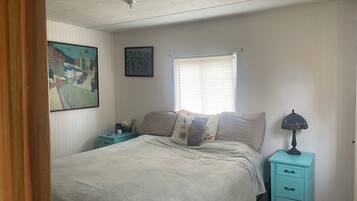 A bedroom with a bed, a nightstand, a lamp, a window with blinds, and two wall-mounted paintings.