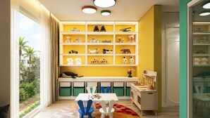 Una stanza giochi per bambini con un'ampia finestra, scaffali pieni di giocattoli, un tavolo con sedie e un tappeto colorato.