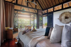 A room with a bed, wicker furniture, and a view of greenery. - Villa Bayu Uluwatu (denpasar)
