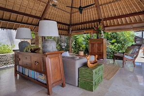 A covered outdoor seating area with a thatched roof, wooden furniture, and lush greenery in the background. - Villa Bayu Uluwatu (denpasar)