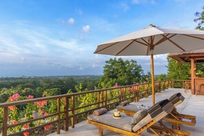 Ein Balkon mit Liegestühlen, einem Sonnenschirm und Blick auf eine üppige Landschaft.