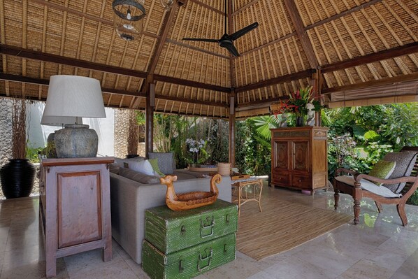 A room with a thatched roof, a ceiling fan, a sofa, a cabinet, a green chest of drawers, and a chair. - Villa Bayu Uluwatu (denpasar)