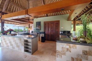 A kitchen with a central island, wooden ceiling beams, and a view of the outdoors. - Villa Bayu Uluwatu (denpasar)