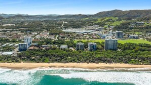A coastal cityscape with high-rise buildings, a beach, and hilly terrain. - Saltbush Beach Pad - Luxe apartment steps to the beach and cafes (Coffs Harbour)