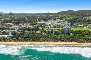A coastal cityscape with high-rise buildings, a beach, and hilly terrain. - Saltbush Beach Pad - Luxe apartment steps to the beach and cafes (Coffs Harbour)