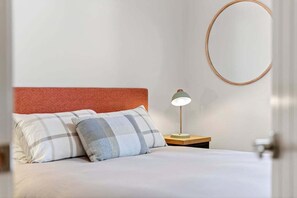 A neatly made bed with two pillows, a bedside lamp, and a round mirror on the wall. - Saltbush Beach Pad - Luxe apartment steps to the beach and cafes (Coffs Harbour)