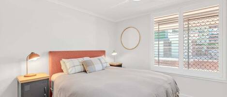 Un dormitorio con cama, mesita de noche, escritorio, ventilador de techo y ventana con persianas.