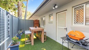 A backyard with a barbecue grill, a wooden table, and potted plants. - Saltbush Beach Pad - Luxe apartment steps to the beach and cafes (Coffs Harbour)