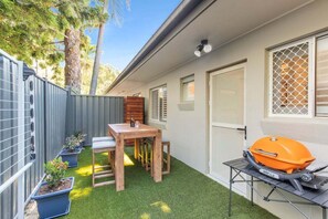 A backyard with a barbecue grill, a wooden table, and potted plants. - Saltbush Beach Pad - Luxe apartment steps to the beach and cafes (Coffs Harbour)