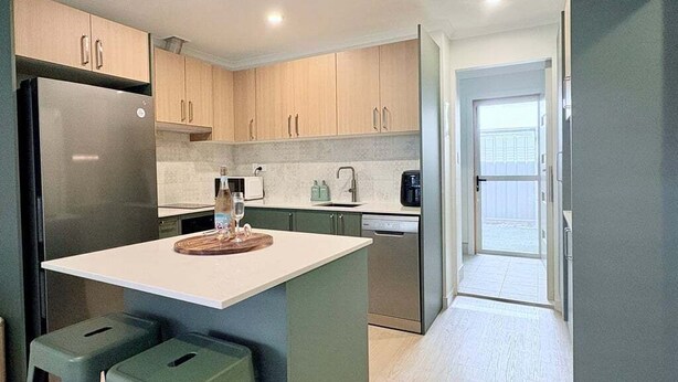 A modern kitchen with a central island, stainless steel appliances, and light wood cabinets. - Saltbush Beach Pad - Luxe apartment steps to the beach and cafes (Coffs Harbour)