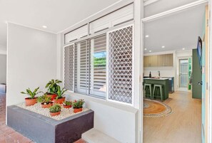 A modern kitchen with a central island, a dining area with a round rug, and a small outdoor planter with plants. - Saltbush Beach Pad - Luxe apartment steps to the beach and cafes (Coffs Harbour)