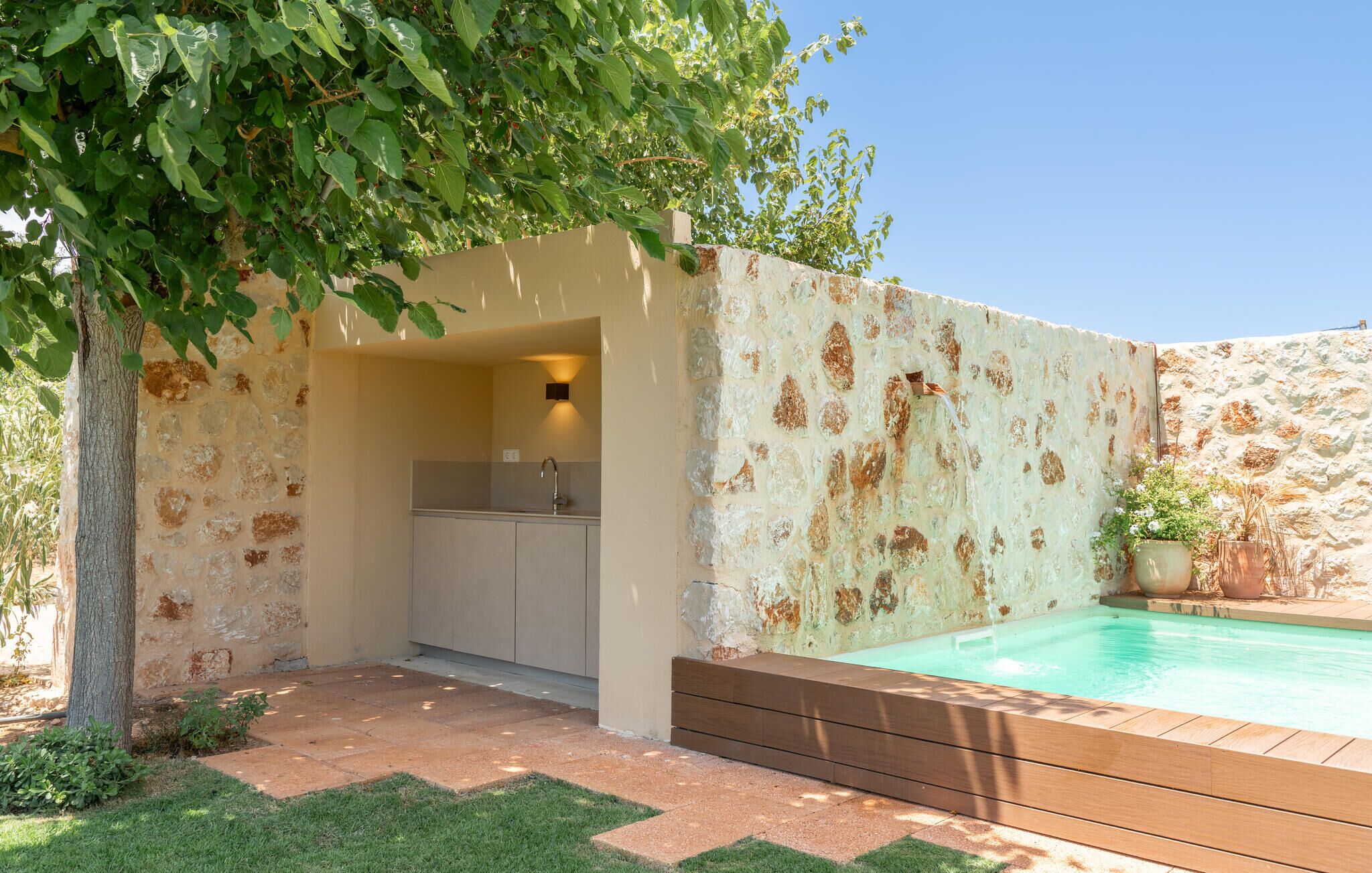 A private pool area with a stone wall, a wooden deck, and a small kitchen with a sink.