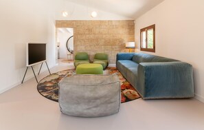 Ein modernes Wohnzimmer mit einem Ecksofa, grünen und grauen Poufs, einem Flachbildfernseher auf einem Lowboard und einer Steinwand.