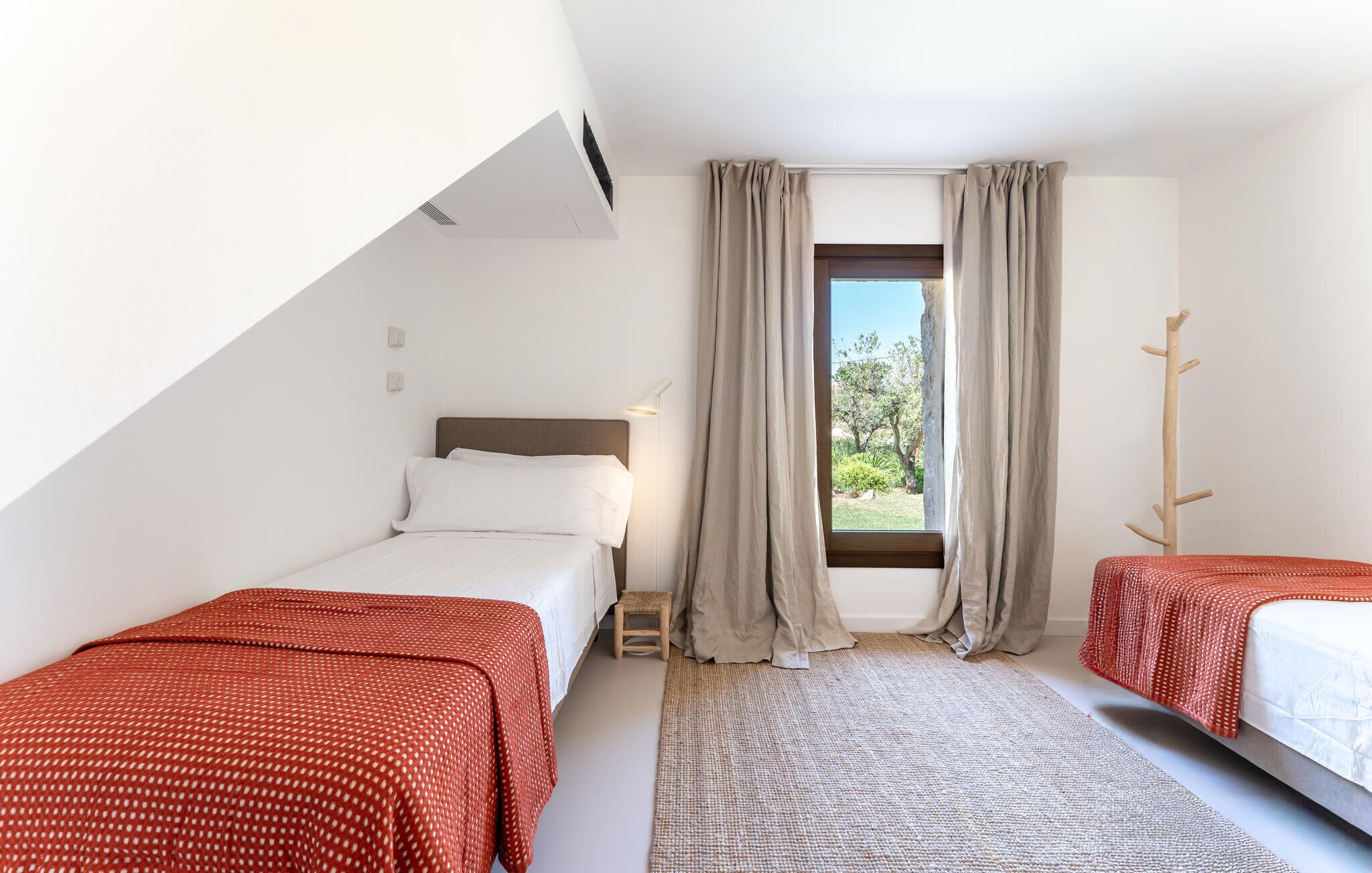 A bedroom with two beds, a window with curtains, a small stool, and a wooden coat rack.