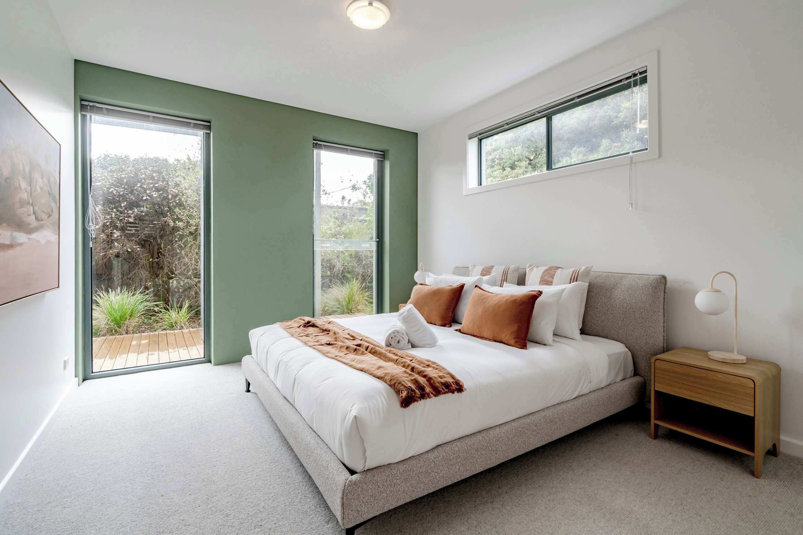 Een moderne slaapkamer met een groot bed, een nachtkastje en een raam met uitzicht op groen.