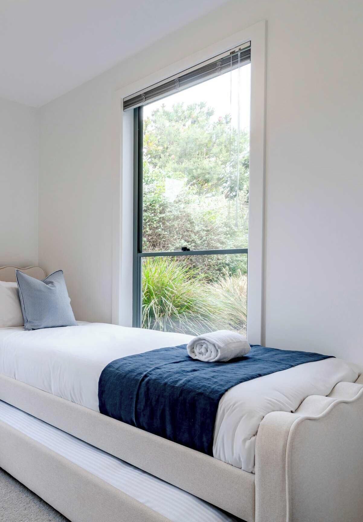 A single bed with a white headboard, a dark blue blanket, and a white pillow.
