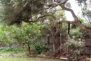 A backyard with a large tree, a swing set, and a wooden fence. - Coastal Elegance in Old Point Lonsdale  Pet Friendly (Point Lonsdale)