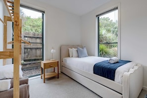 A bedroom with a bed, bedside table, lamp, and a view of greenery through large windows. - Coastal Elegance in Old Point Lonsdale  Pet Friendly (Point Lonsdale)