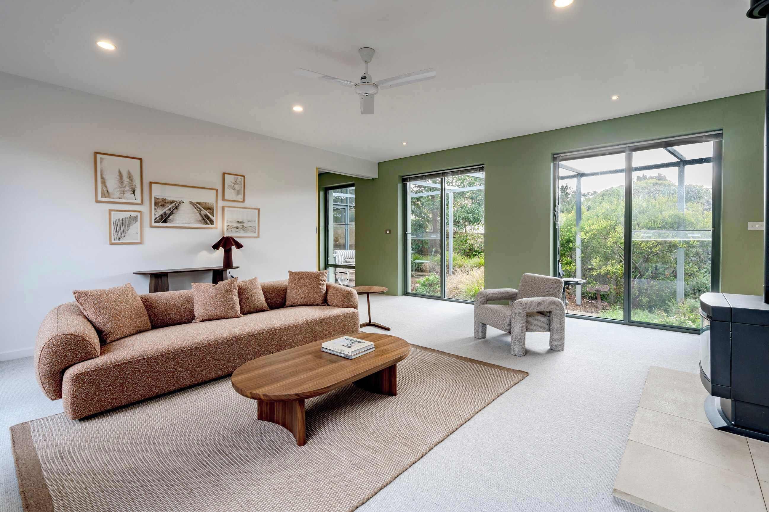 A modern living room with a sofa, coffee table, and armchairs, large windows, and artwork on the walls.