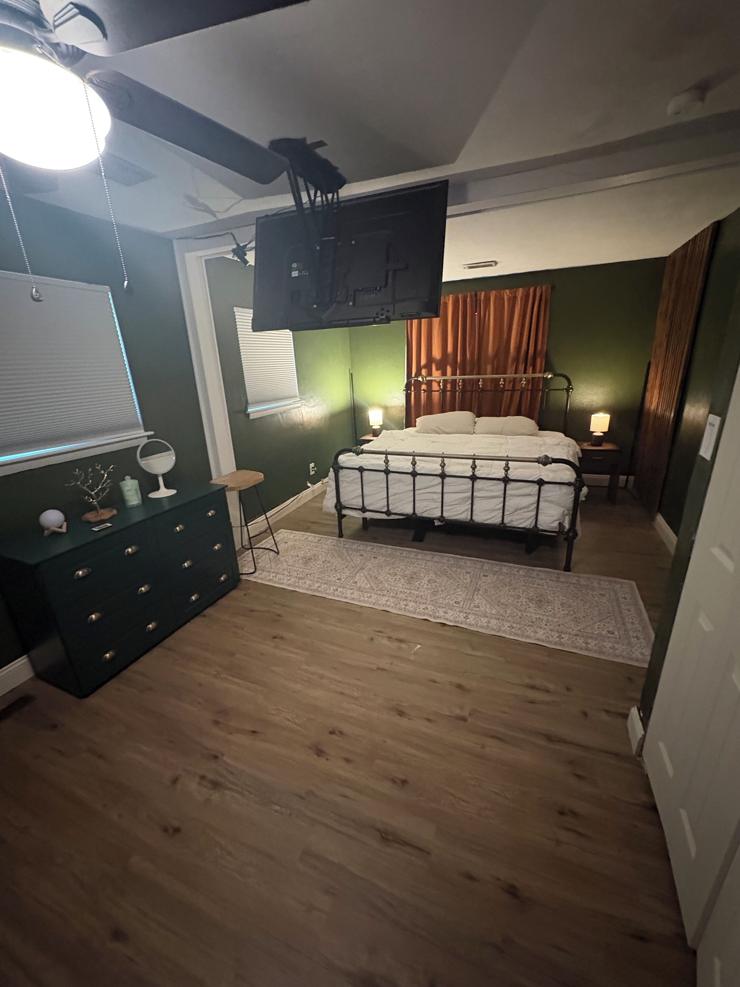 A bedroom with a bed, a dresser, a television, and a window with curtains.