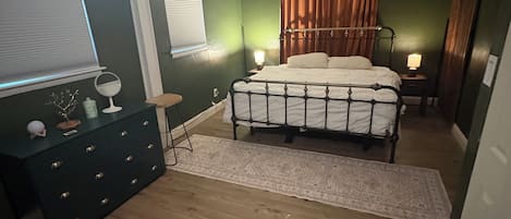 A bedroom with a bed, a dresser, a television, and a window with curtains.