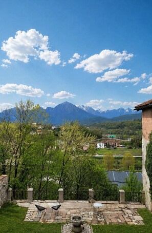 A patio with stone flooring, a stone wall, and a view of mountains and a village. - 101 - Fireplace Room (Belluno)