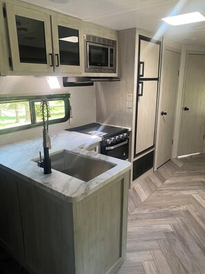 A compact kitchen with a built-in microwave, a stove, and a sink. - Cozy  1-bedroom recreational vehicle with views close to Kalispell. (Kalispell)