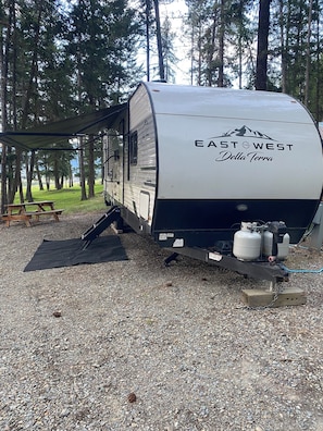 A recreational vehicle with 'EAST WEST Della Terra' branding, a picnic table, and propane tanks. - Cozy  1-bedroom recreational vehicle with views close to Kalispell. (Kalispell)