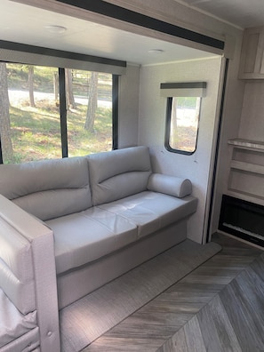A modern RV interior with a sectional sofa, large windows, and a fireplace. - Cozy  1-bedroom recreational vehicle with views close to Kalispell. (Kalispell)