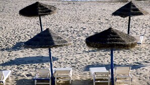 En strand med parasoller av halmtak och vita solstolar.