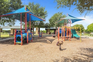 A playground with slides and climbing structures, surrounded by trees and a clear sky. - 3BR Sanctuary: Clean, Cozy & Complete with Pools and 20 min to DT Austin (Mustang Ridge)