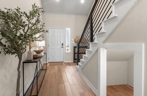 A hallway with a wooden floor, a white door, a staircase with white railings, and a plant on a console table. - 3BR Sanctuary: Clean, Cozy & Complete with Pools and 20 min to DT Austin (Mustang Ridge)