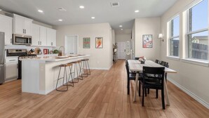A modern kitchen with white cabinets, a central island with stools, and a dining area with a table and chairs. - 3BR Sanctuary: Clean, Cozy & Complete with Pools and 20 min to DT Austin (Mustang Ridge)
