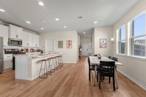 A modern kitchen with white cabinets, a central island with stools, and a dining area with a table and chairs. - 3BR Sanctuary: Clean, Cozy & Complete with Pools and 20 min to DT Austin (Mustang Ridge)