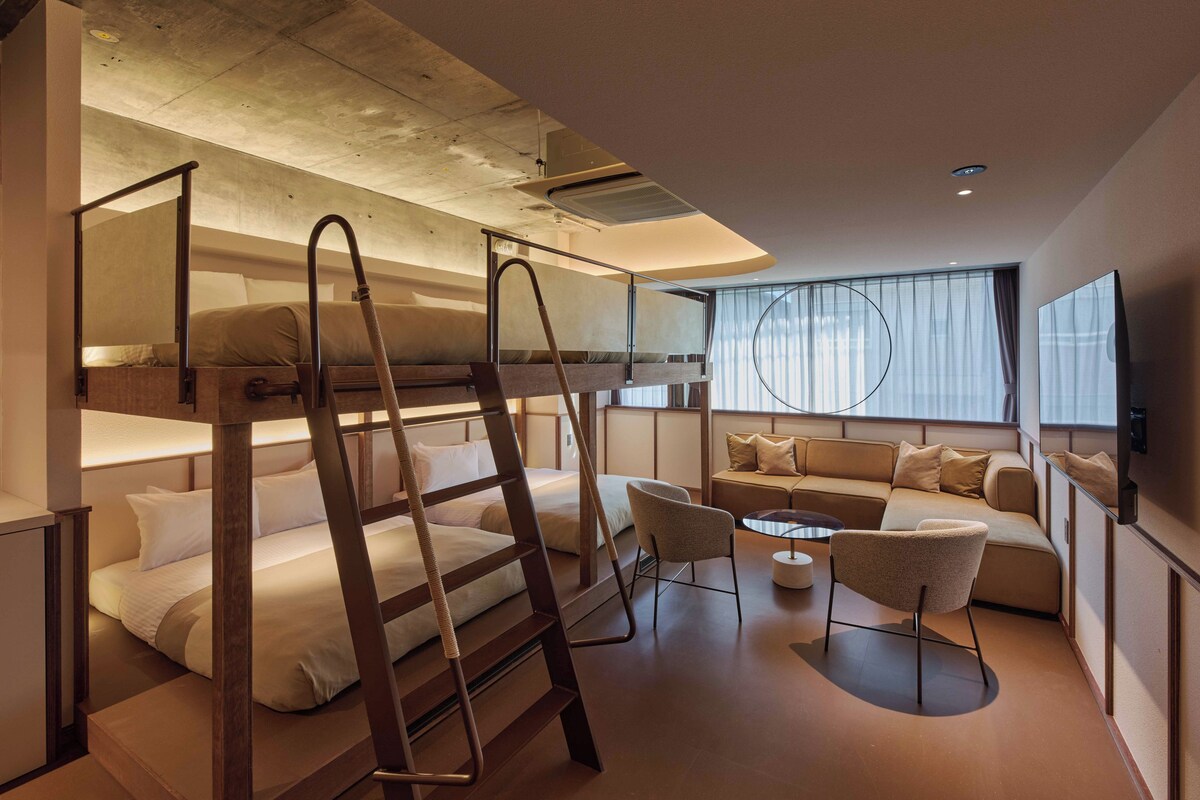 Una habitación de hotel moderna con literas, un sofá, una mesita y un televisor.
