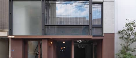 A modern building with a glass facade, a visible staircase, and a small tree in the foreground.