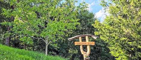 A wooden signpost with directional arrows and the text 'RANNER-HOF' in a natural setting with trees and grass.