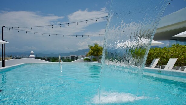 Uma piscina com um recurso aquático, rodeada por espreguiçadeiras e uma guirlanda de luzes.