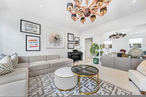 Ein modernes Wohnzimmer mit einer Eckcouch, einem Glastisch und Kunstwerken an den Wänden.