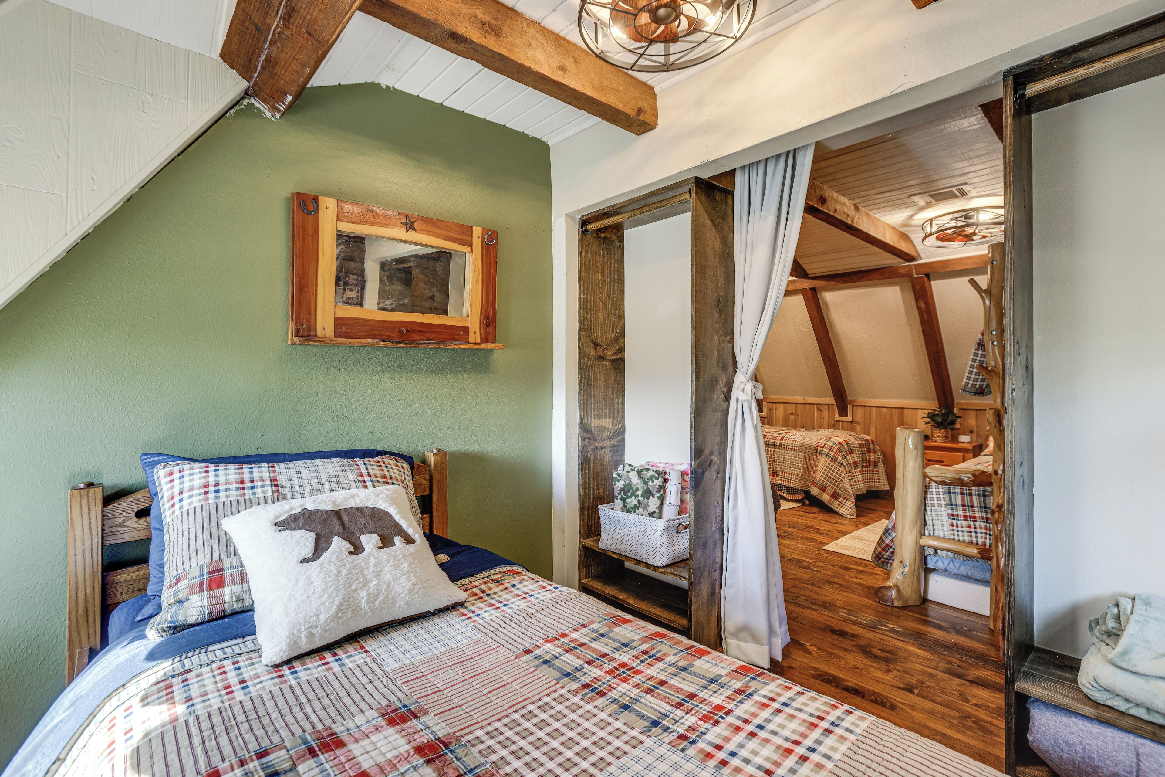 A cozy bedroom with a bed, a wooden headboard, a green wall, a wooden ceiling, and a window with curtains.